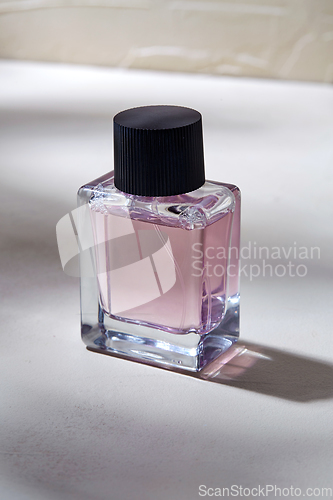 Image of bottle of perfume on white surface with shadows