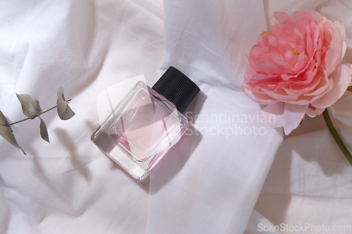 Image of bottle of perfume and flower on white sheet