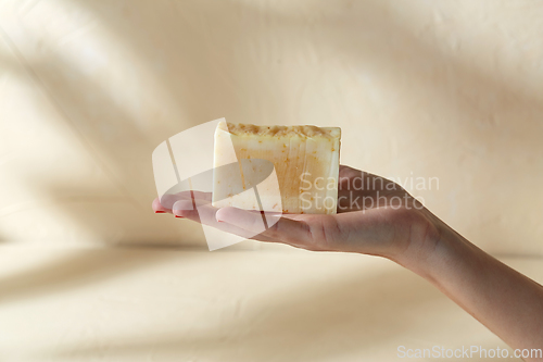 Image of hand holding bar of craft soap on beige background