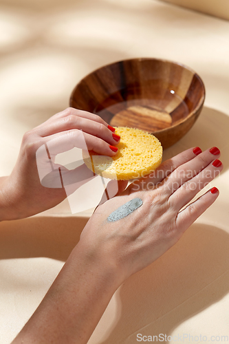 Image of hands applying blue cosmetic clay mask to skin