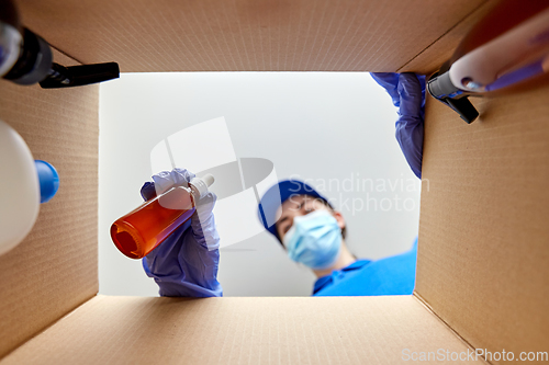 Image of woman in mask packing parcel box with cosmetics