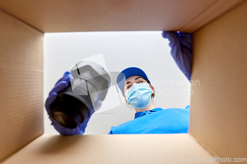 Image of woman in mask packing camera into parcel box