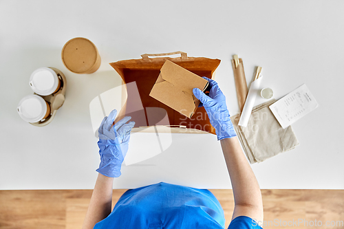 Image of delivery woman in gloves packing food and drinks