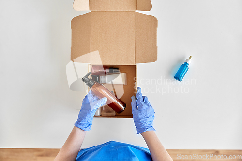 Image of hands in gloves packing parcel box with cosmetics