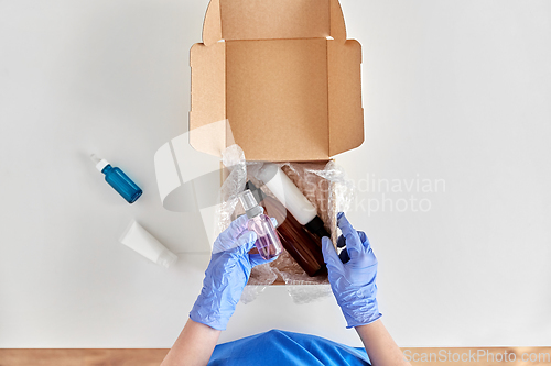 Image of hands in gloves packing parcel box with cosmetics