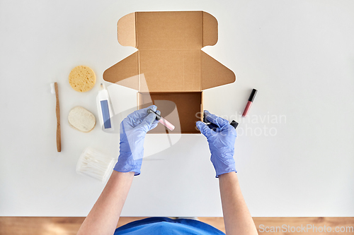 Image of hands in gloves packing parcel box with cosmetics