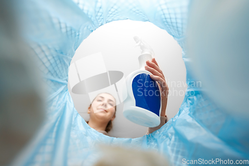 Image of woman throwing bottle of detergent into trash can