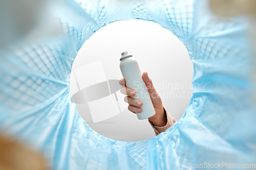 Image of hand throwing hair spray bottle into trash can