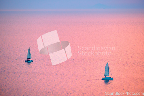 Image of Tourist yachts boat in Aegean sea near Santorini island with tourists watching sunset viewpoint. Santorini, Greece