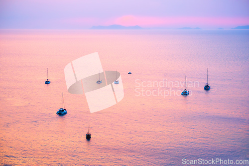 Image of Tourist yachts boat in Aegean sea near Santorini island with tourists watching sunset viewpoint. Santorini, Greece