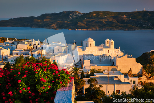 Image of View of Plaka village on Milos island over red geranium flowers on sunset in Greece