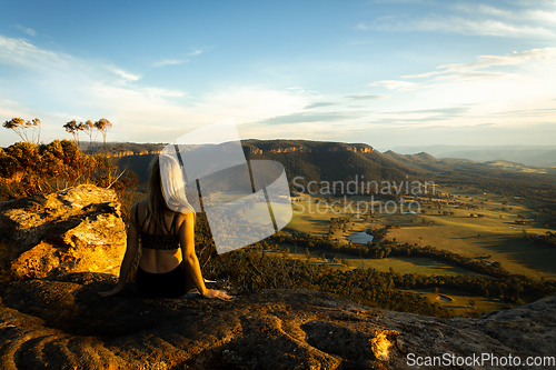 Image of Female sitting high on a cliff look out over sunlit valley