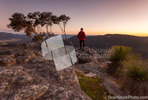 Image of Woman standing on rocky mountain  ledge at sunset