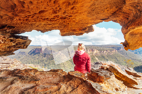 Image of Woman sits in sandstone cave with a spectacular mountain view