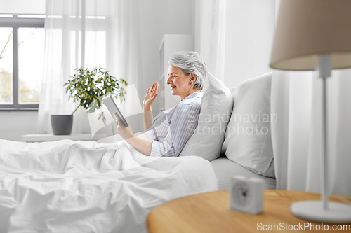 Image of old woman with tablet pc having video call in bed