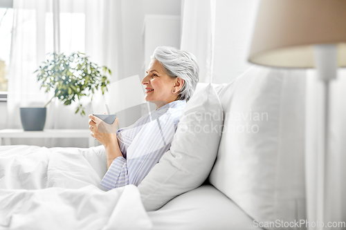 Image of old woman with cup of coffee in bed at home