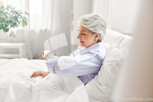 Image of happy senior woman sitting in bed at home bedroom