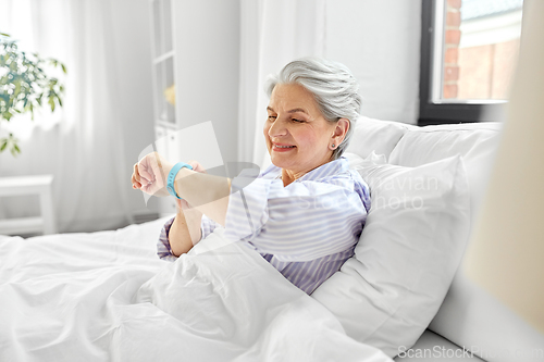 Image of happy old woman with health tracker sitting in bed