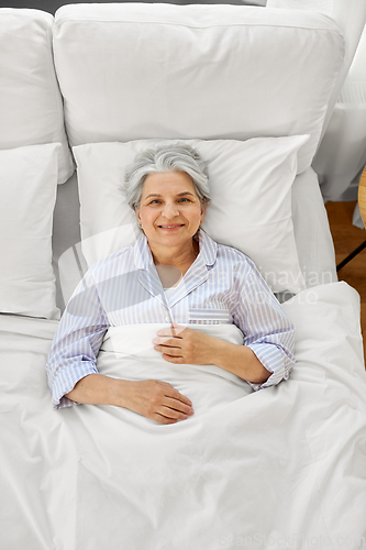 Image of smiling senior woman lying in bed at home bedroom