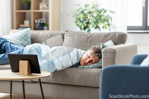 Image of bored man with tablet pc lying on sofa at home