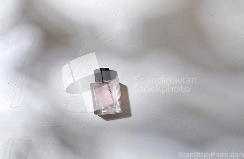 Image of bottle of perfume on white surface with shadows