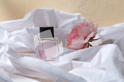 Image of bottle of perfume and flower on white sheet