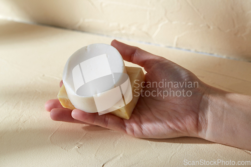 Image of hand holding bar of craft soap on beige background