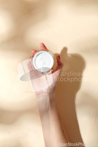 Image of female hand holding jar of moisturizer