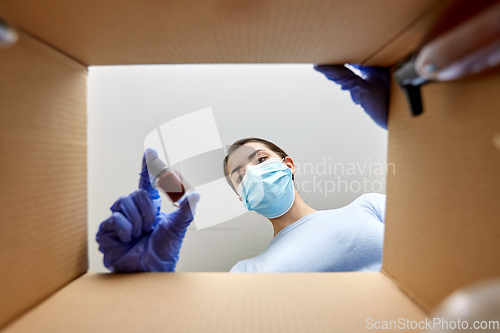 Image of woman in mask unpacking parcel box with cosmetics