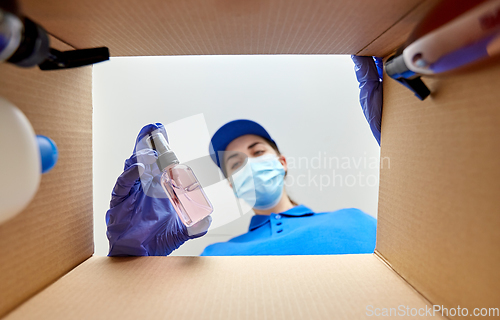 Image of woman in mask packing parcel box with cosmetics