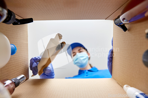 Image of woman in mask packing parcel box with cosmetics