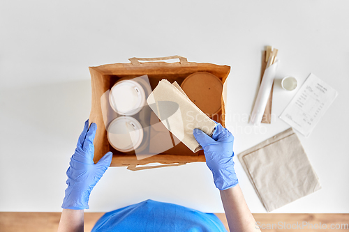 Image of delivery woman in gloves packing food and drinks