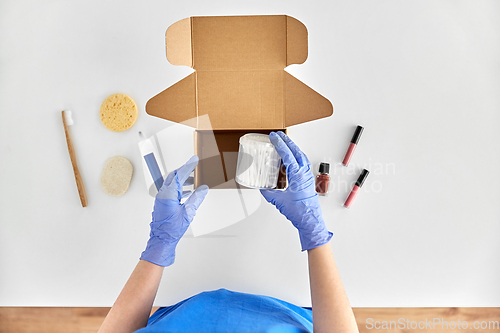 Image of hands in gloves packing parcel box with cosmetics