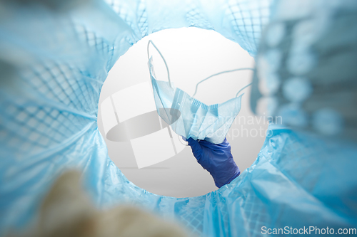 Image of hand throwing used medical mask into trash can