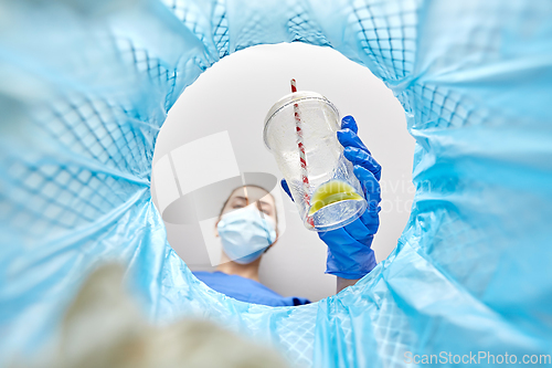 Image of female doctor throwing plastic cup into trash can