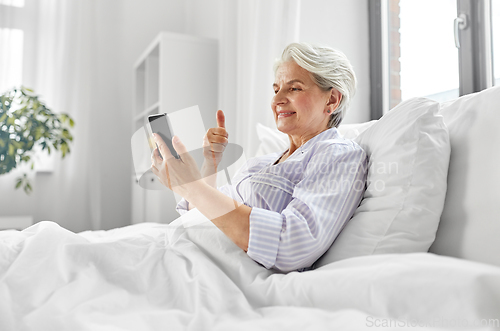 Image of senior woman with phone having video call in bed