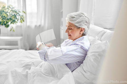 Image of happy senior woman sitting in bed at home bedroom