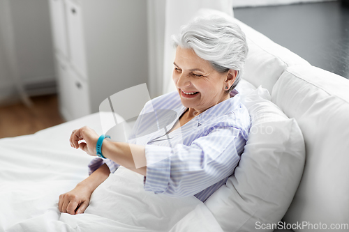 Image of happy old woman with health tracker sitting in bed