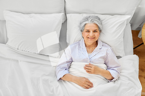 Image of smiling senior woman lying in bed at home bedroom