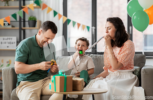 Image of happy family with gifts and party blowers at home