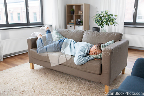 Image of bored or lazy young man lying on sofa at home