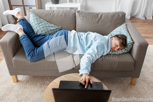 Image of bored man with laptop lying on sofa at home