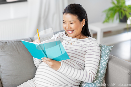 Image of happy pregnant woman writing to diary at home