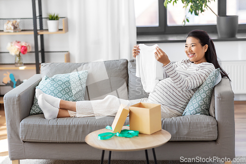 Image of happy pregnant woman with baby's bodysuit at home