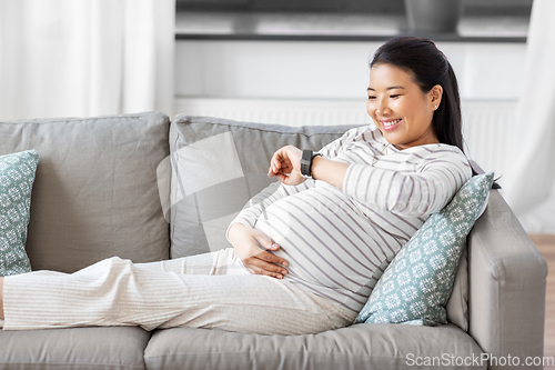 Image of happy pregnant woman with smart watch at home