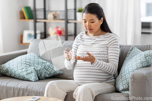 Image of pregnant woman with glucometer making blood test