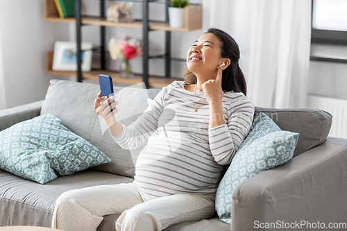 Image of pregnant woman with phone and earphones at home