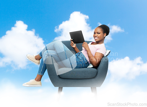 Image of smiling woman with tablet pc sitting in armchair