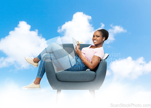 Image of happy young woman in armchair writing to notebook