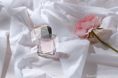 Image of bottle of perfume and flower on white sheet